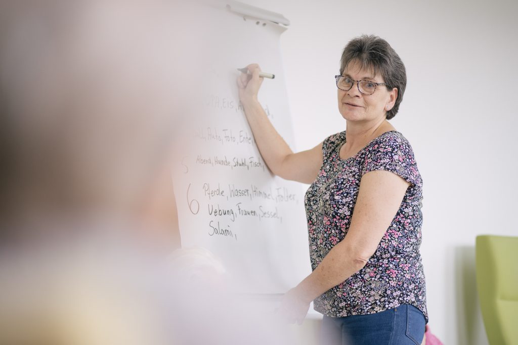Eine Frau schreibt etwas mit einem Stift an ein Flipchart und guckt in unsere Richtung.